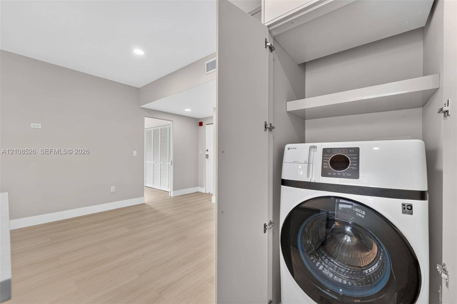 Built-in laundry closet with recessed shelving, wood-finish flooring, and crisp neutral wall paint