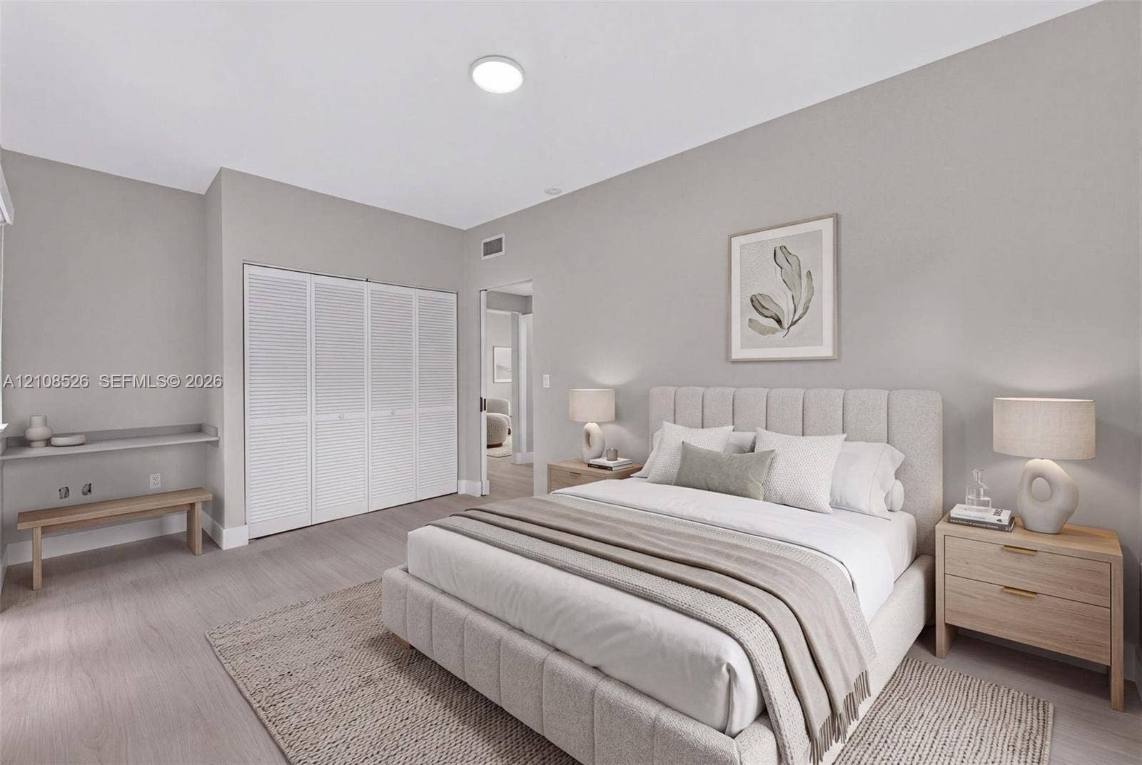 Neutral-toned interior space featuring light-toned wood-finish flooring, floor-to-ceiling white louvered closet doors, and a built-in floating desk surface