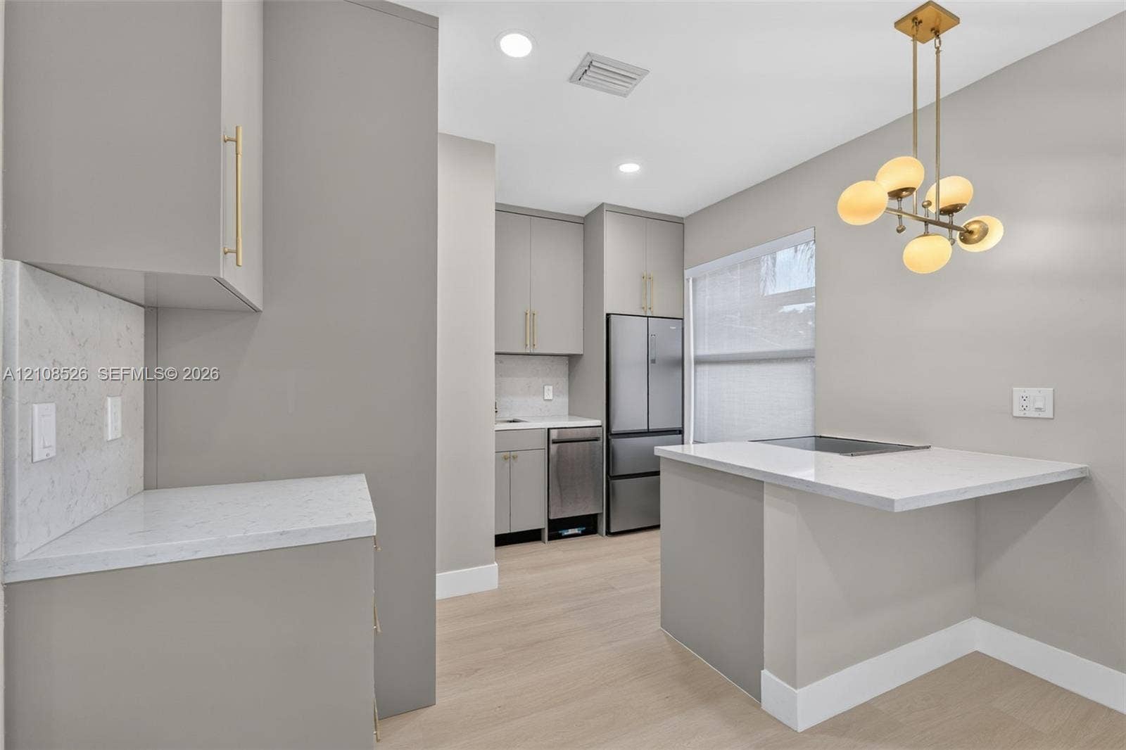 Kitchen featuring flat-panel cabinetry with gold-tone hardware, stone countertops, stainless steel appliances, wood-finish flooring, and a multi-globe pendant light fixture