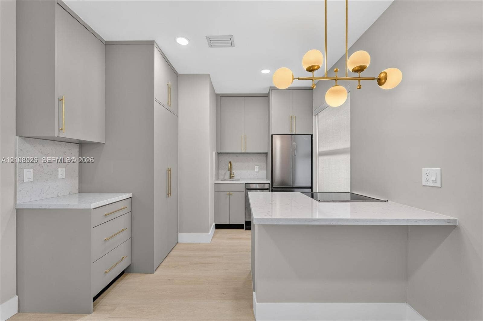 Kitchen featuring light gray cabinetry with gold-tone hardware, white stone-finish countertops, wood-finish flooring, and a multi-globe pendant light fixture