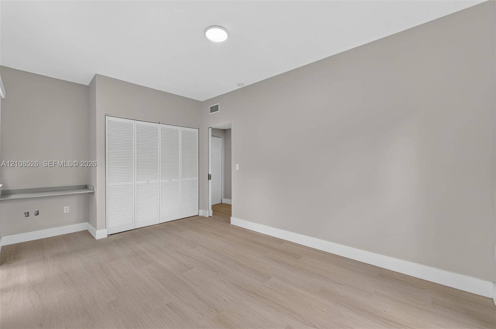 Neutral-toned interior space featuring wood-finish flooring, white louvered closet doors, and a built-in floating desk