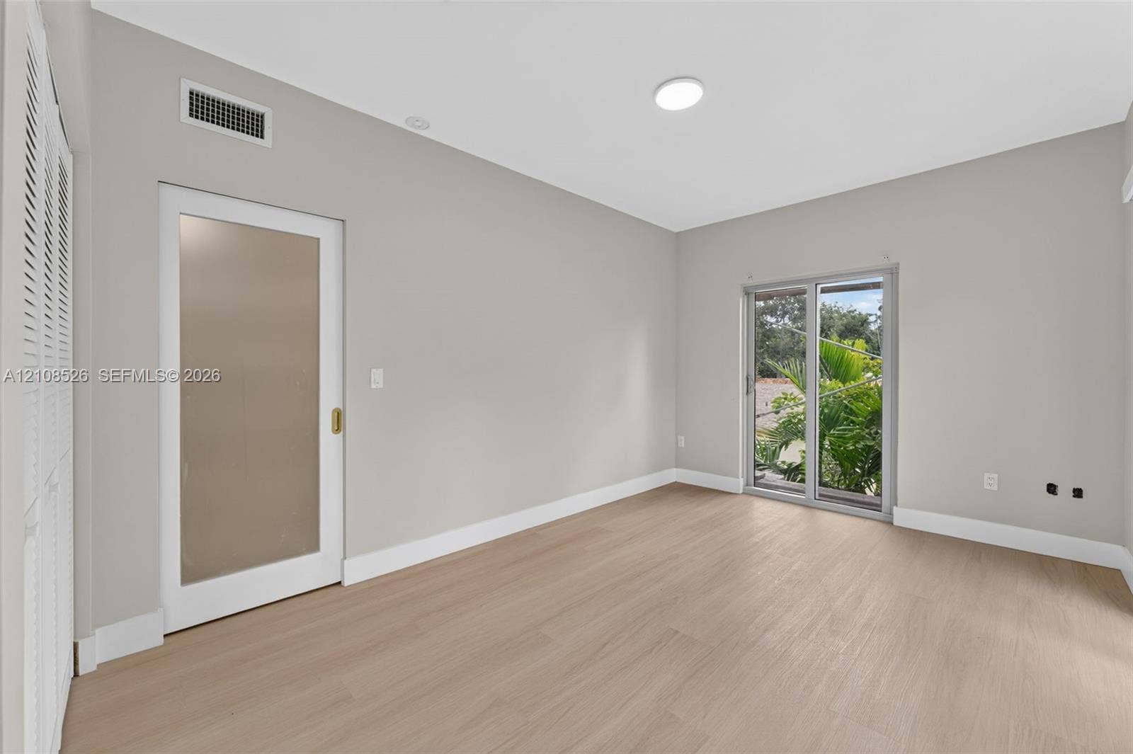 Light-filled room featuring wood-finish flooring, a sliding glass door with exterior greenery, and a frosted glass panel door