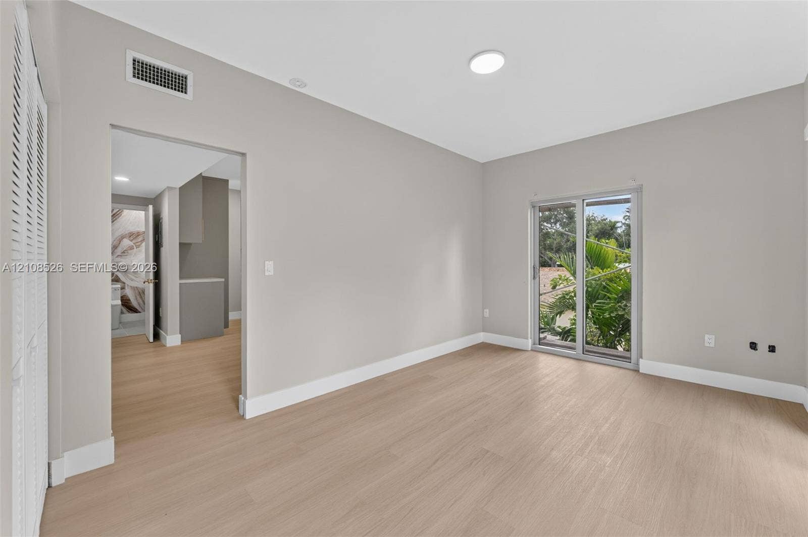 Neutral-toned interior featuring wood-finish flooring, sliding glass doors, and louvered closet doors