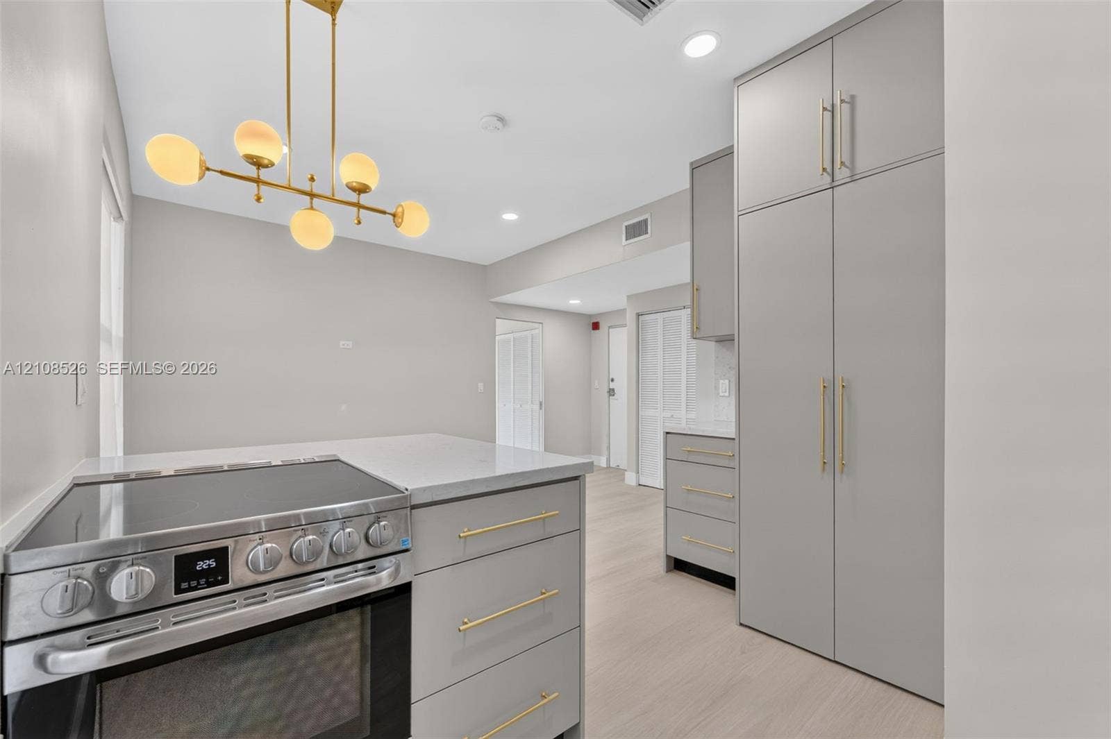 Kitchen featuring light gray cabinetry, brushed gold hardware, a stainless steel slide-in range, quartz countertops, and a multi-globe pendant light fixture