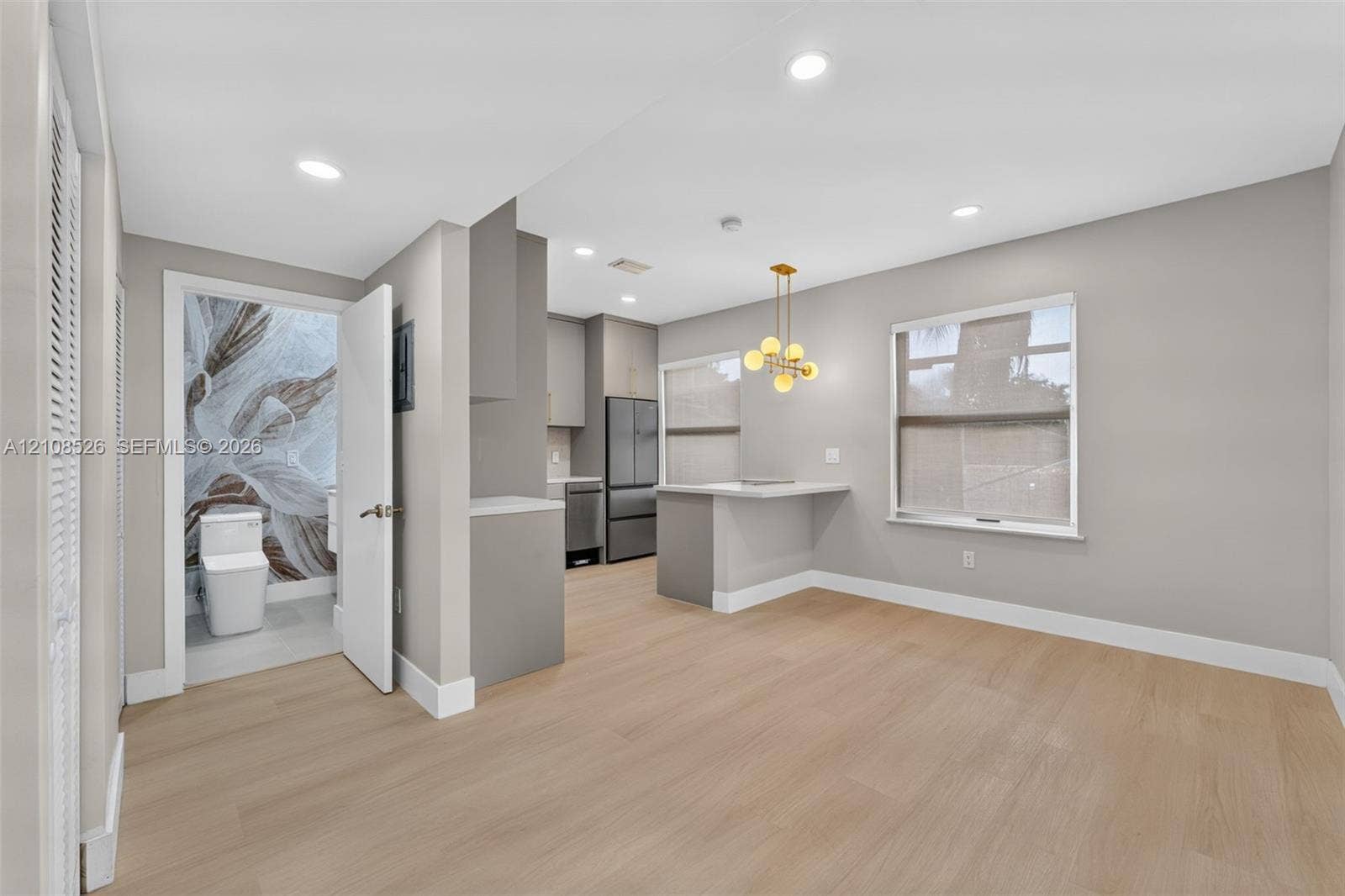 Open-concept interior featuring light wood-finish flooring, recessed lighting, a kitchen peninsula with integrated counter seating, and a modern multi-globe chandelier