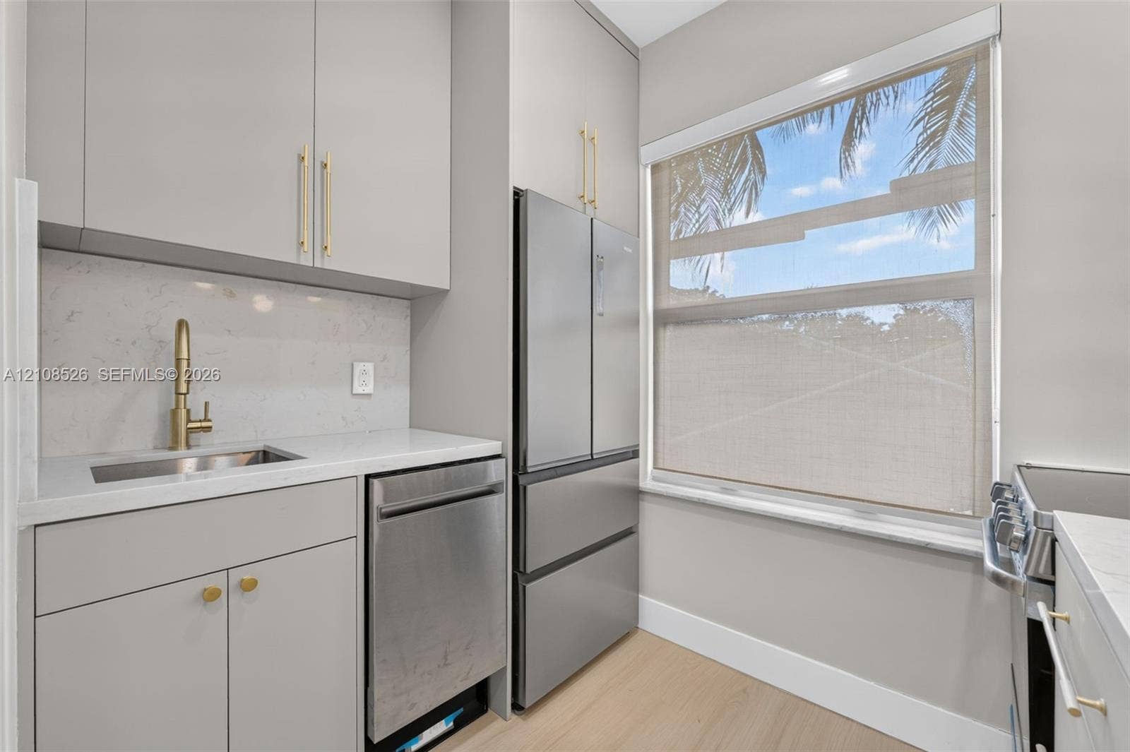 Kitchenette featuring flat-panel cabinetry, light-toned stone-finish countertops, stainless steel appliances, a gold-toned faucet, and wood-finish flooring