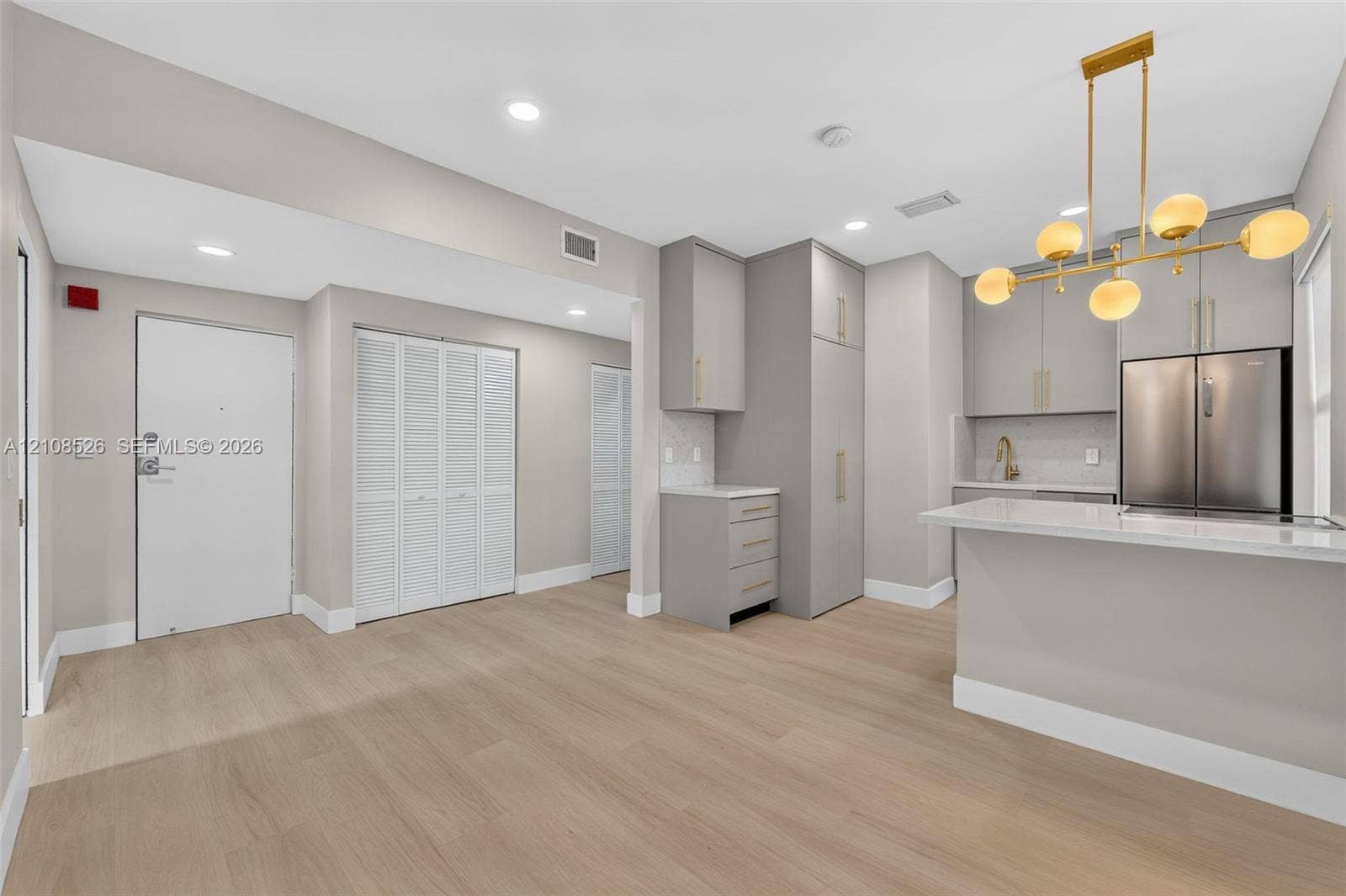 Kitchen featuring custom grey cabinetry, quartz countertops, a stainless steel refrigerator, recessed lighting, and wood-finish flooring