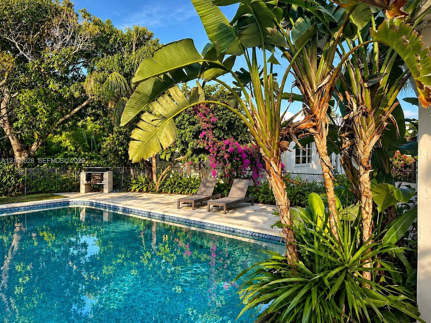 1124 N 18th Avenue N, Lake Worth, FL 33460 In-ground swimming pool with tiled water-line, stone paver patio, and built-in masonry barbecue station, complemented by mature tropical landscaping