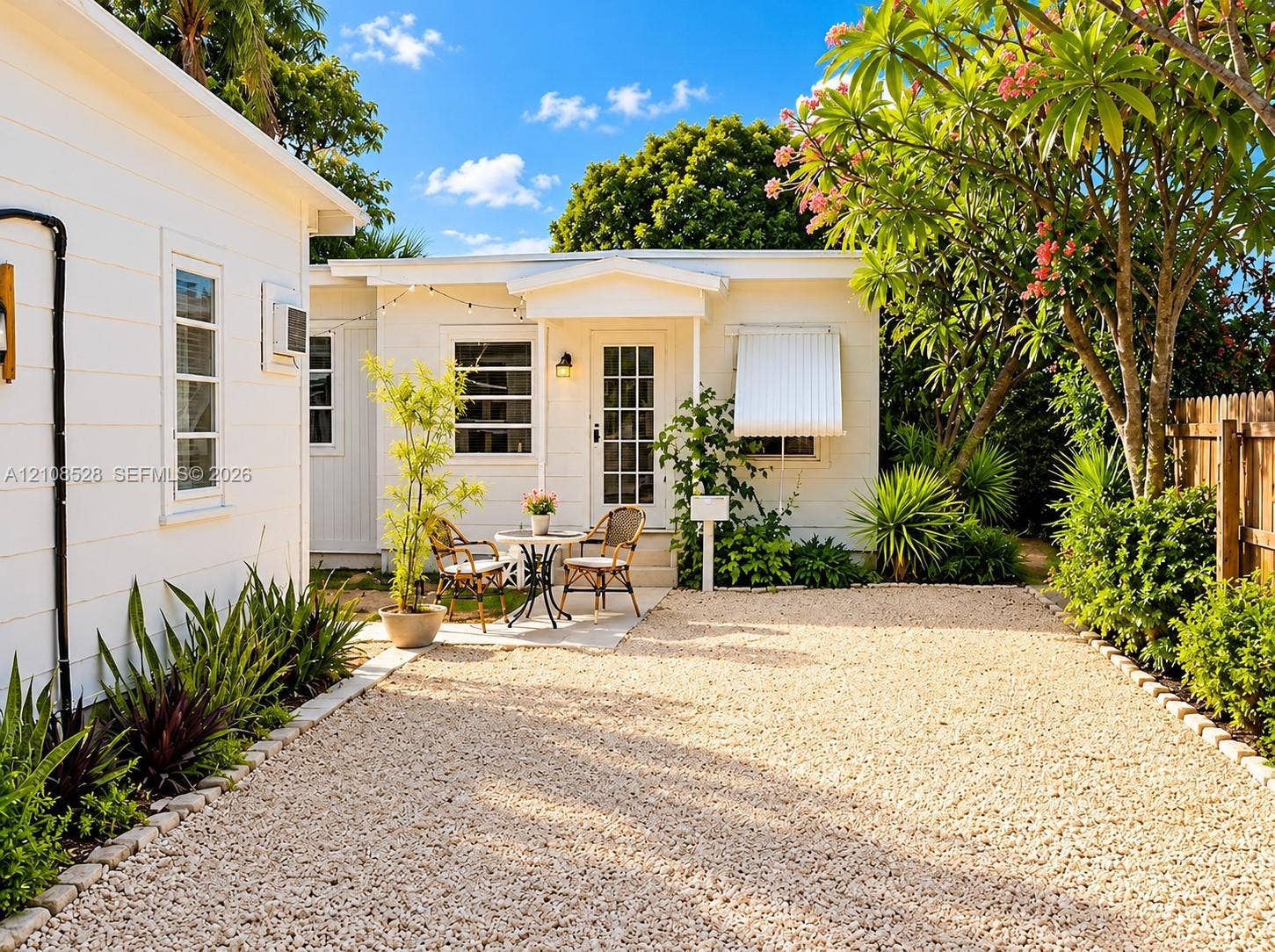 1124 N 18th Avenue N, Lake Worth, FL 33460 White horizontal siding exterior featuring a gravel courtyard, mature landscaping, and a glass-paneled entry door