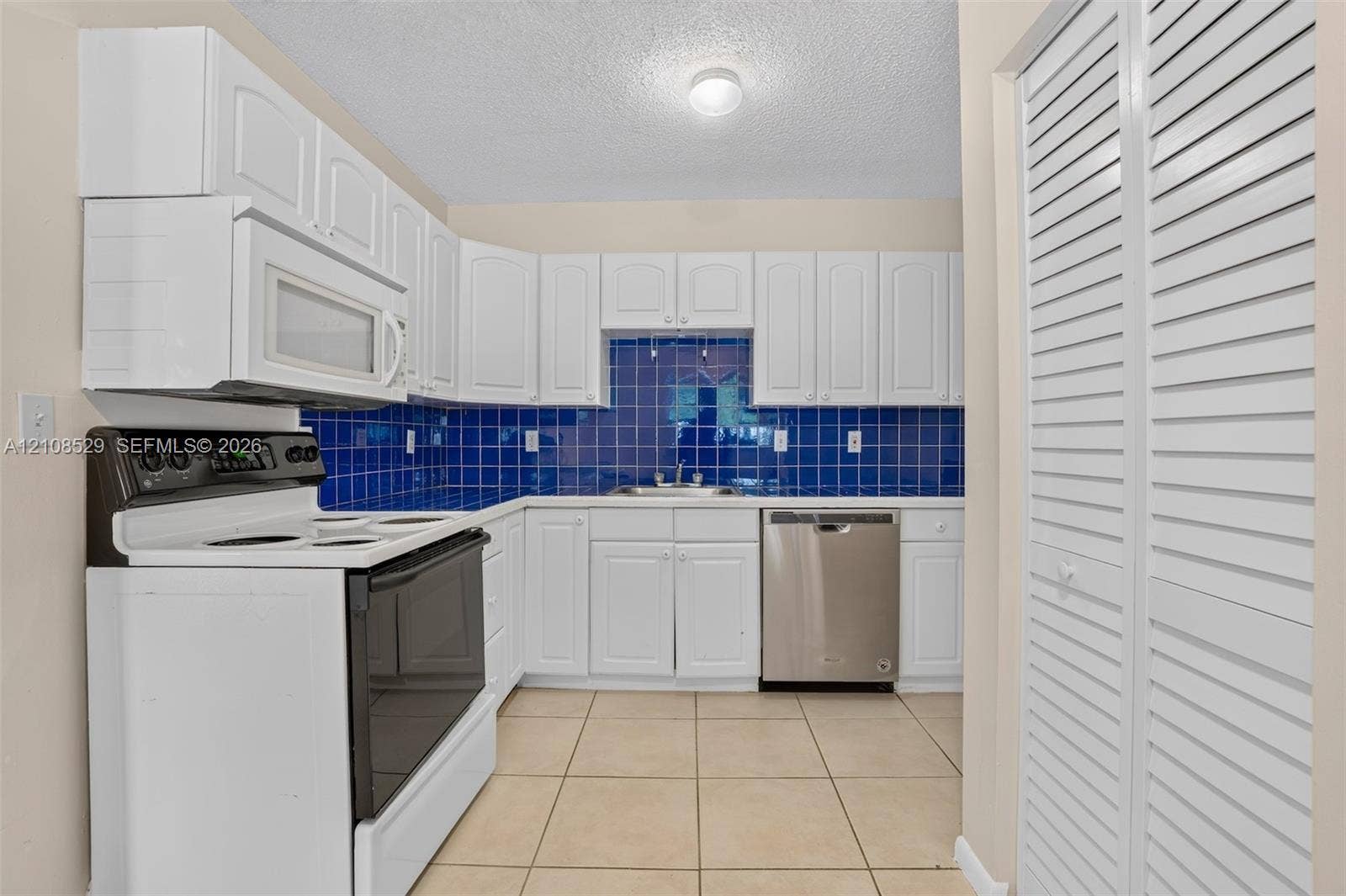 1015 SW 4th Avenue, #A, Fort Lauderdale, Fort Lauderdale, FL 33315 Kitchen featuring white cabinetry, blue tiled backsplash, stainless steel dishwasher, built-in microwave, and tile flooring