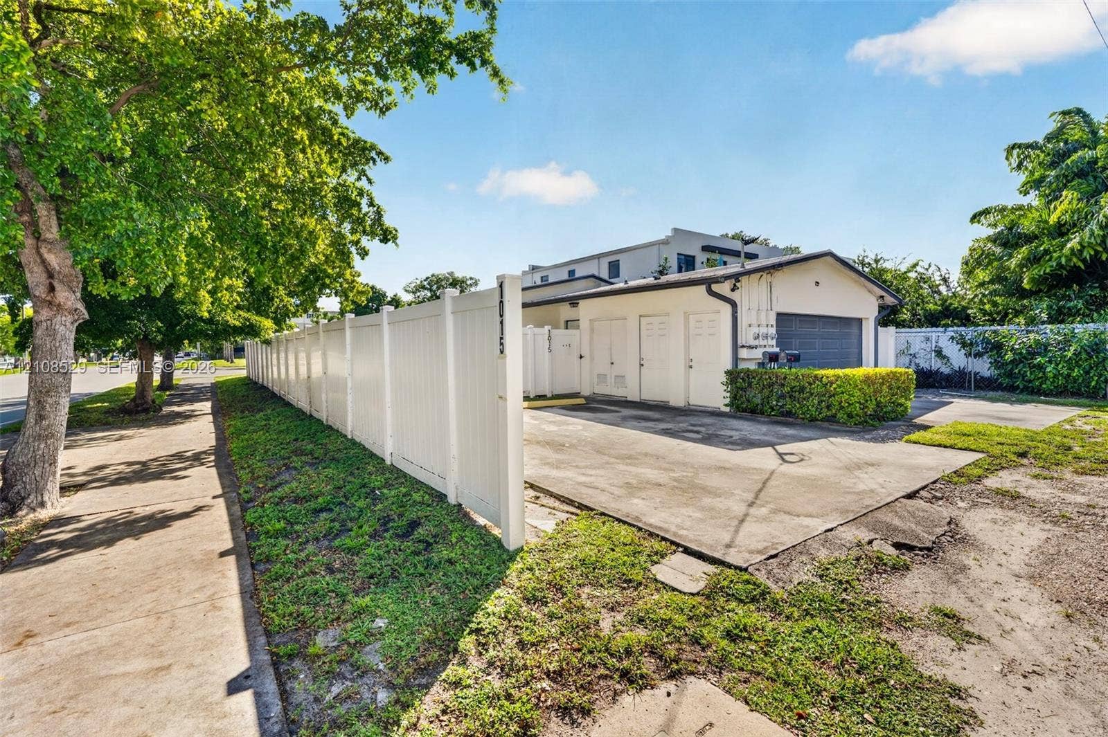 1015 SW 4th Avenue, #A, Fort Lauderdale, Fort Lauderdale, FL 33315 Concrete driveway leading to a multi-bay structure featuring a detached garage with solid-panel doors, secured by a white vinyl privacy fence