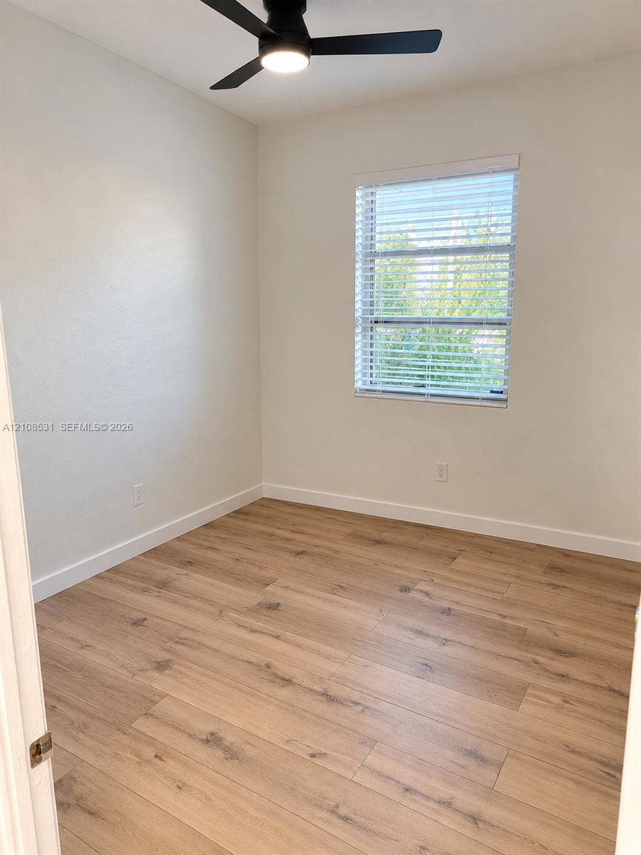 3024 Clyde Road, #1, West Palm Beach, West Palm Beach, FL 33405 Room featuring wood-finish flooring, a matte black ceiling fan with integrated lighting, and a single-pane window with white horizontal blinds