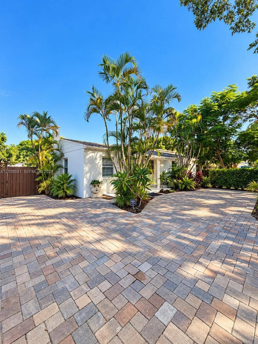 3024 Clyde Road, #1, West Palm Beach, West Palm Beach, FL 33405 Exterior facade featuring white painted siding, expansive paver driveway, mature palm trees, and perimeter privacy fencing