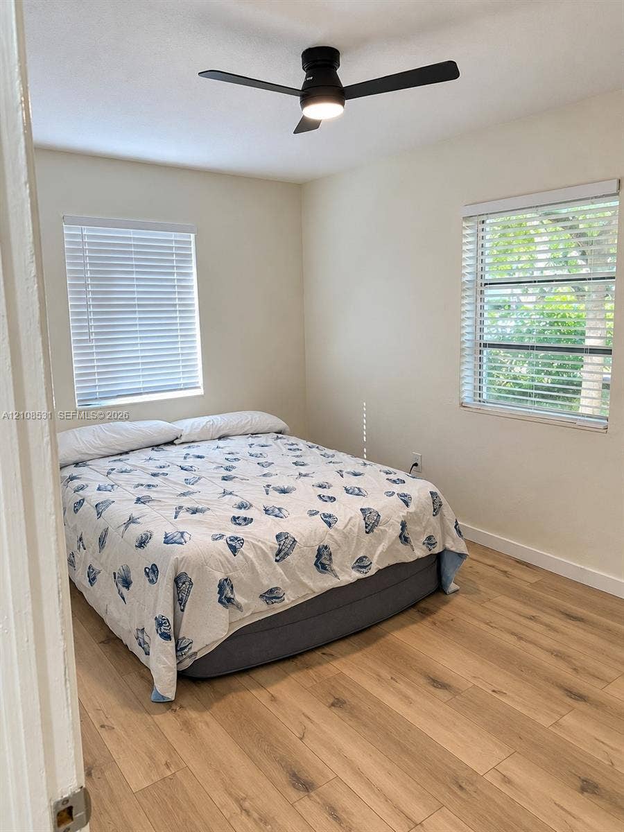 3024 Clyde Road, #1, West Palm Beach, West Palm Beach, FL 33405 Neutral interior featuring light-tone wood-finish flooring, dual windows with horizontal blinds, and a modern matte black ceiling fan with integrated lighting