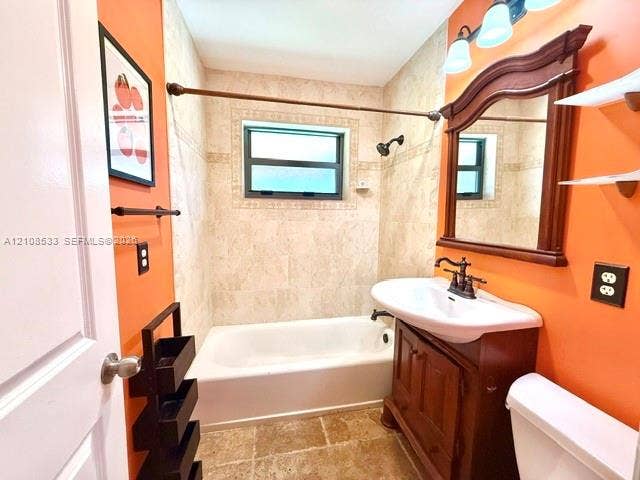 1124 NE 7th Street, Hallandale Beach, Hallandale Beach, FL 33009 Bathroom featuring a vanity with an integrated basin, wall-mounted wooden-frame mirror, stone-tiled shower surround with decorative inlay, tile flooring, and three-light wall fixture