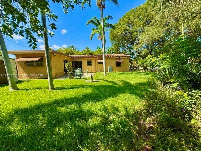 1124 NE 7th Street, Hallandale Beach, Hallandale Beach, FL 33009 Rear exterior featuring a stucco facade, tile roof, concrete patio, and mature palm trees within a landscaped lawn