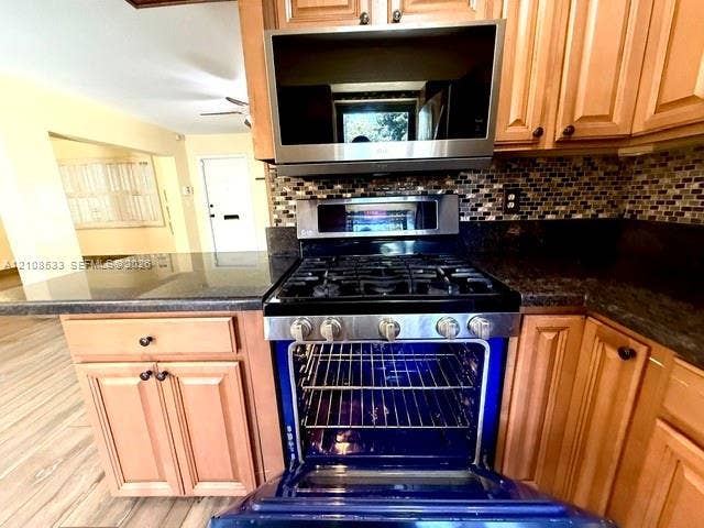 1124 NE 7th Street, Hallandale Beach, Hallandale Beach, FL 33009 Kitchen featuring stained wood cabinetry, stone countertops, stainless steel gas range with convection oven, built-in microwave, and mosaic tile backsplash
