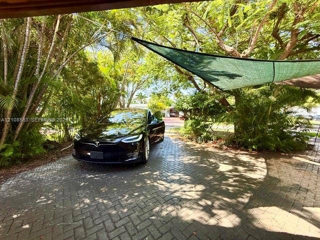 1124 NE 7th Street, Hallandale Beach, Hallandale Beach, FL 33009 Herringbone-patterned paver driveway featuring mature tropical landscaping and a fixed overhead shade canopy