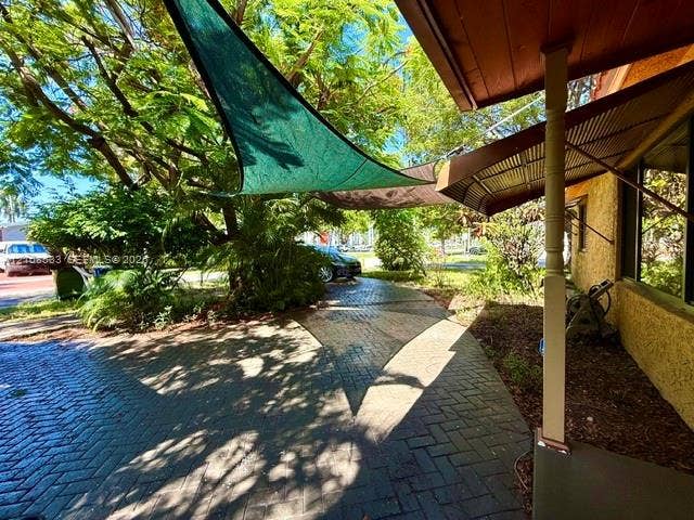 1124 NE 7th Street, Hallandale Beach, Hallandale Beach, FL 33009 Herringbone-patterned brick paver patio featuring a fixed porch support column, metal awning, and triangular overhead shade sails