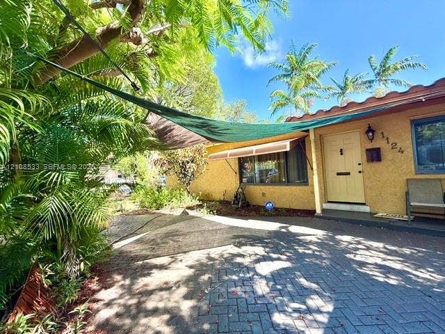 1124 NE 7th Street, Hallandale Beach, Hallandale Beach, FL 33009 Stucco exterior featuring a terracotta-tile roofline, brick-paver driveway, and exterior wall-mounted lighting