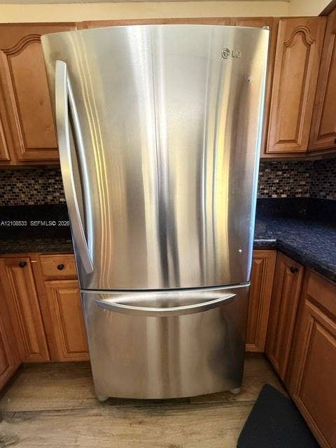 1124 NE 7th Street, Hallandale Beach, Hallandale Beach, FL 33009 Stainless steel bottom-freezer refrigerator, dark-toned stone countertops, multi-colored mosaic tile backsplash, and wood-finish cabinetry
