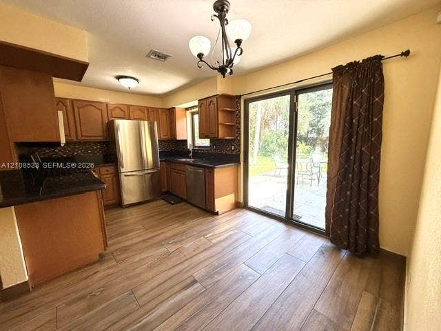 1124 NE 7th Street, Hallandale Beach, Hallandale Beach, FL 33009 Kitchen featuring wood-finish flooring, dark stone countertops, stainless steel appliances, decorative light fixtures, and a glass sliding door
