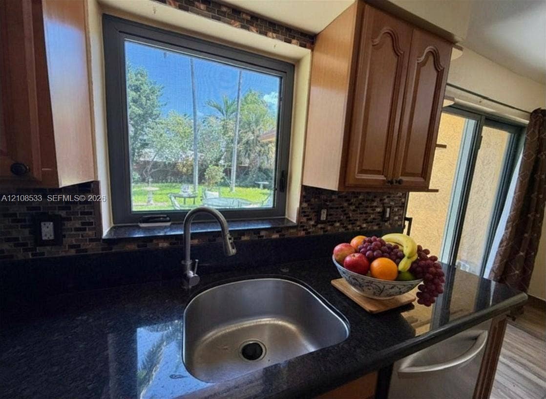 1124 NE 7th Street, Hallandale Beach, Hallandale Beach, FL 33009 Kitchen featuring dark stone countertops, mosaic tile backsplash, wood-finish cabinetry, stainless steel undermount sink with high-arc faucet, and oversized window