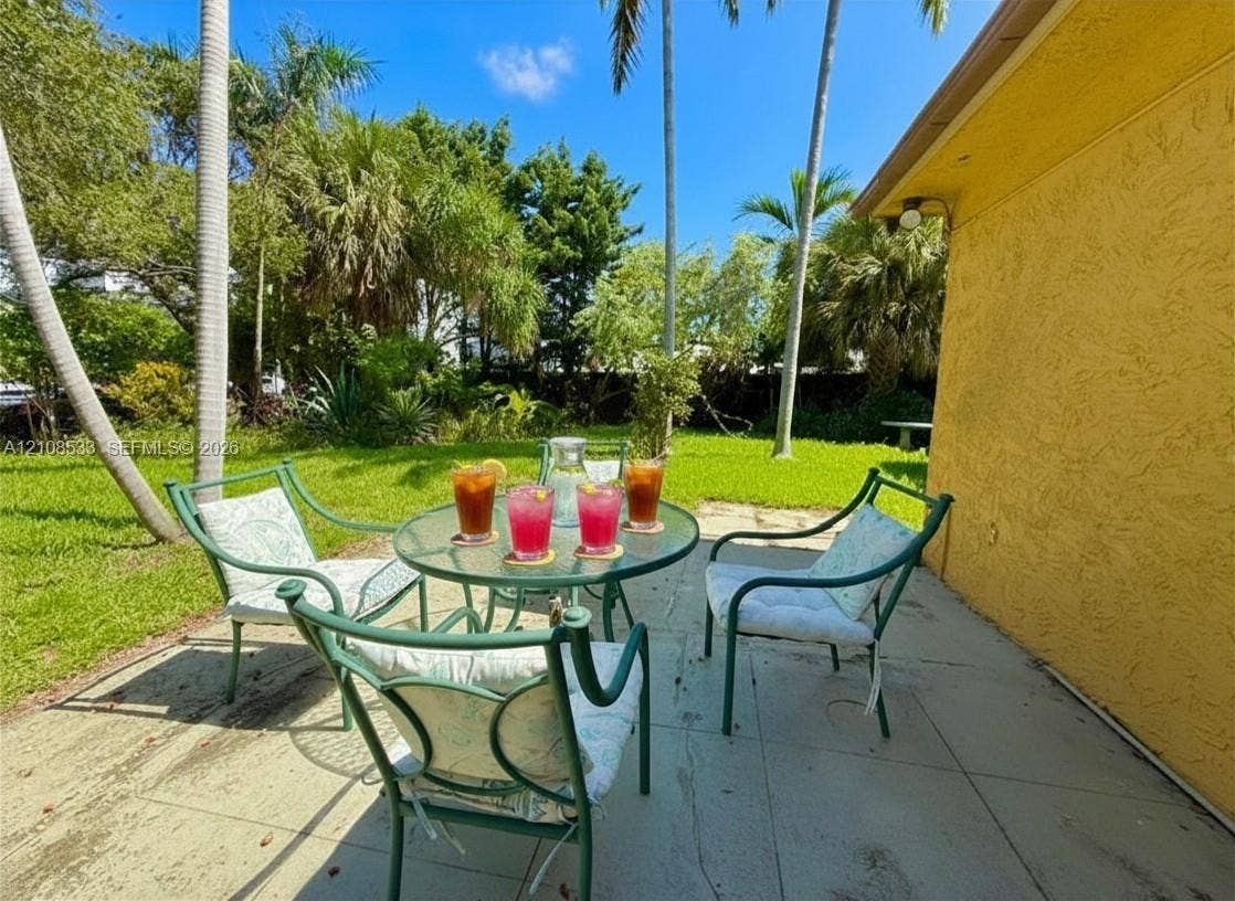 1124 NE 7th Street, Hallandale Beach, Hallandale Beach, FL 33009 Rear patio featuring a concrete surface, texturized exterior wall, and established landscaping with palm trees