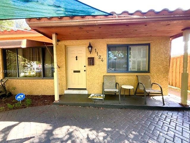 1124 NE 7th Street, Hallandale Beach, Hallandale Beach, FL 33009 Stucco exterior entry featuring a covered porch, herringbone-patterned brick paver driveway, solid-core front door, and mission-style roof tiles