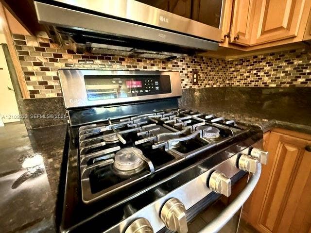 1124 NE 7th Street, Hallandale Beach, Hallandale Beach, FL 33009 Stainless steel gas range with a built-in microwave, dark stone countertops, mosaic tile backsplash, and wood-finish cabinetry