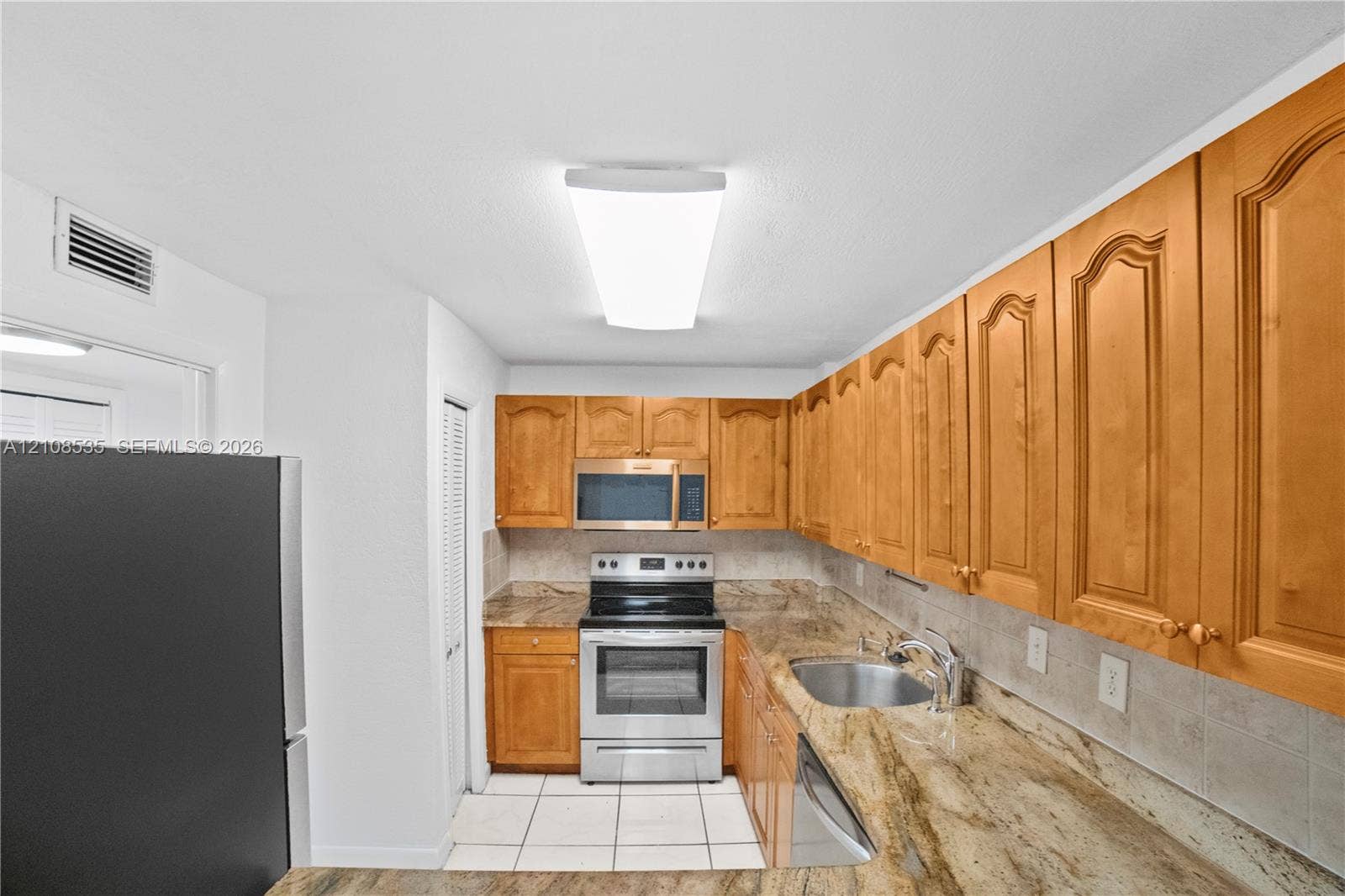 Kitchen featuring natural wood cabinetry, stone-surface countertops, tile backsplash, stainless steel appliances, and ceramic tile flooring