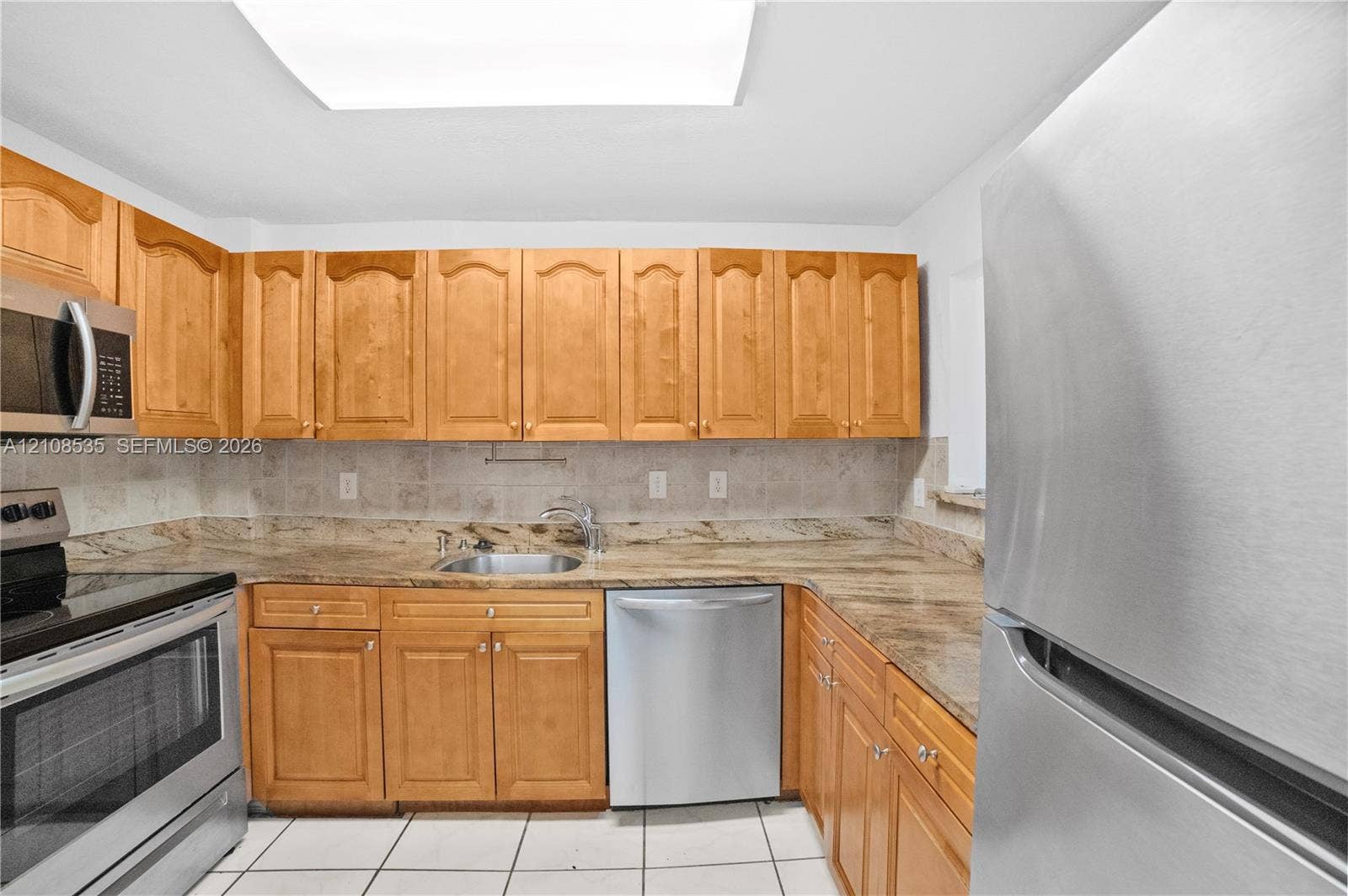 Kitchen featuring natural wood cabinetry, stone-surface countertops, tile backsplash, stainless steel appliances, and tile flooring