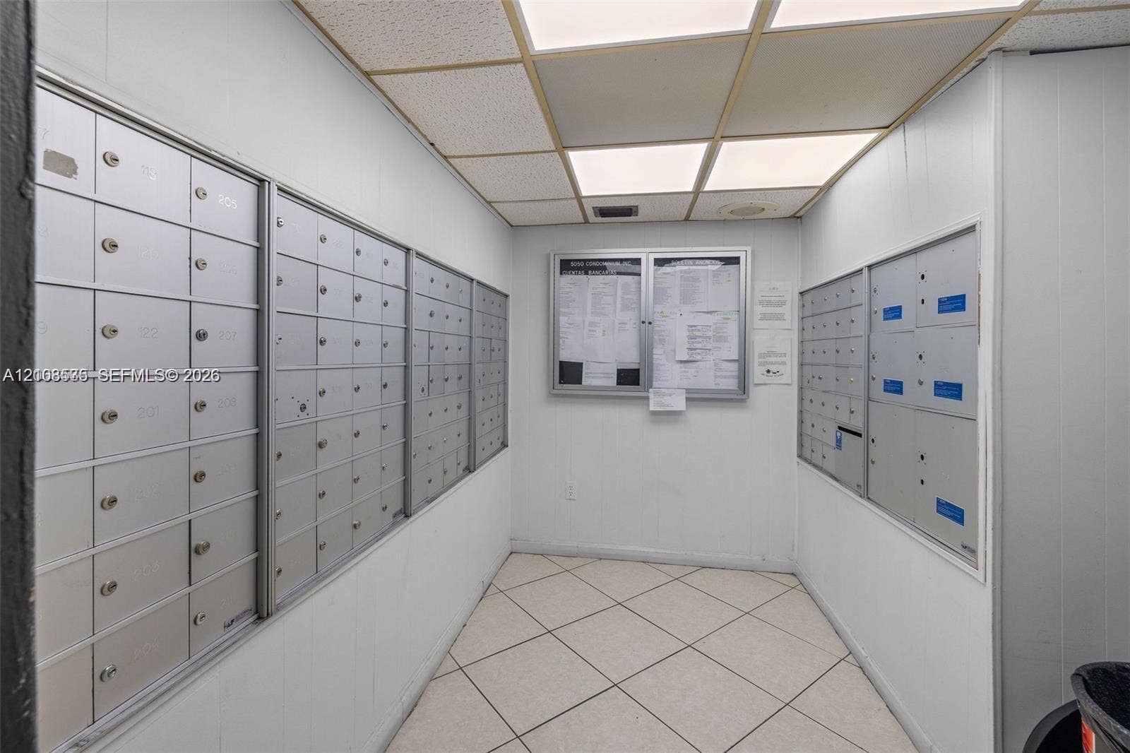 Mailroom featuring wall-mounted metal mailboxes, drop-ceiling panel lighting, and diagonal tile flooring
