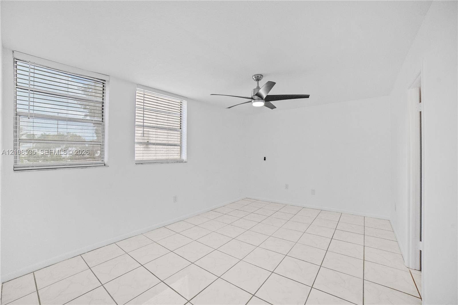 Interior space featuring white tile flooring, neutral walls, two horizontal-slat windows, and a brushed-nickel ceiling fan with integrated lighting