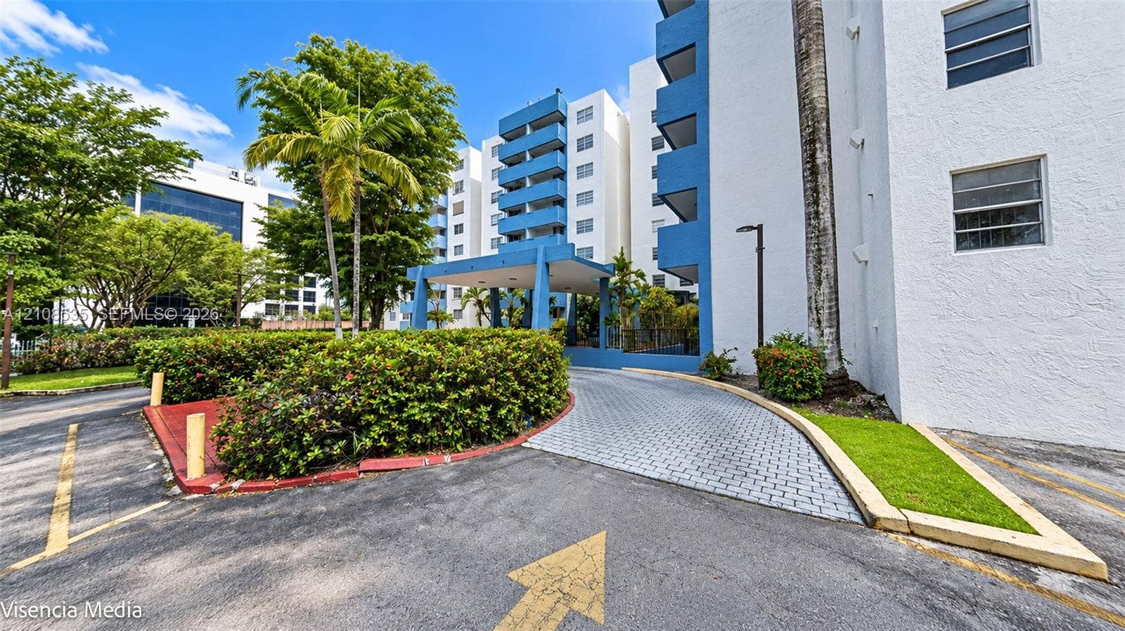 Multi-story exterior featuring a covered entryway, paved driveway, blue structural accents, and landscaped grounds