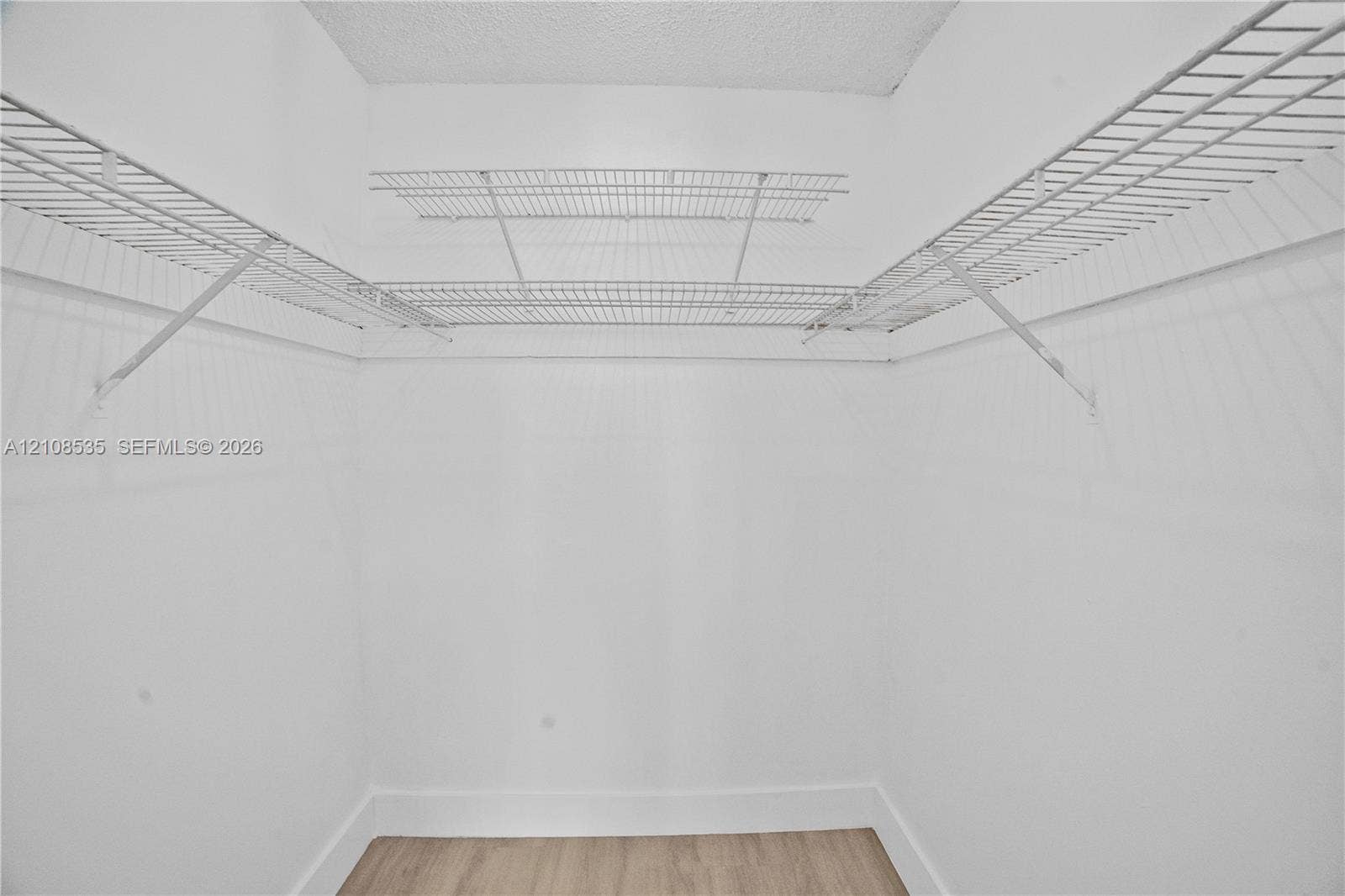 Storage space featuring dual-tier white wire shelving and light-toned wood-finish flooring