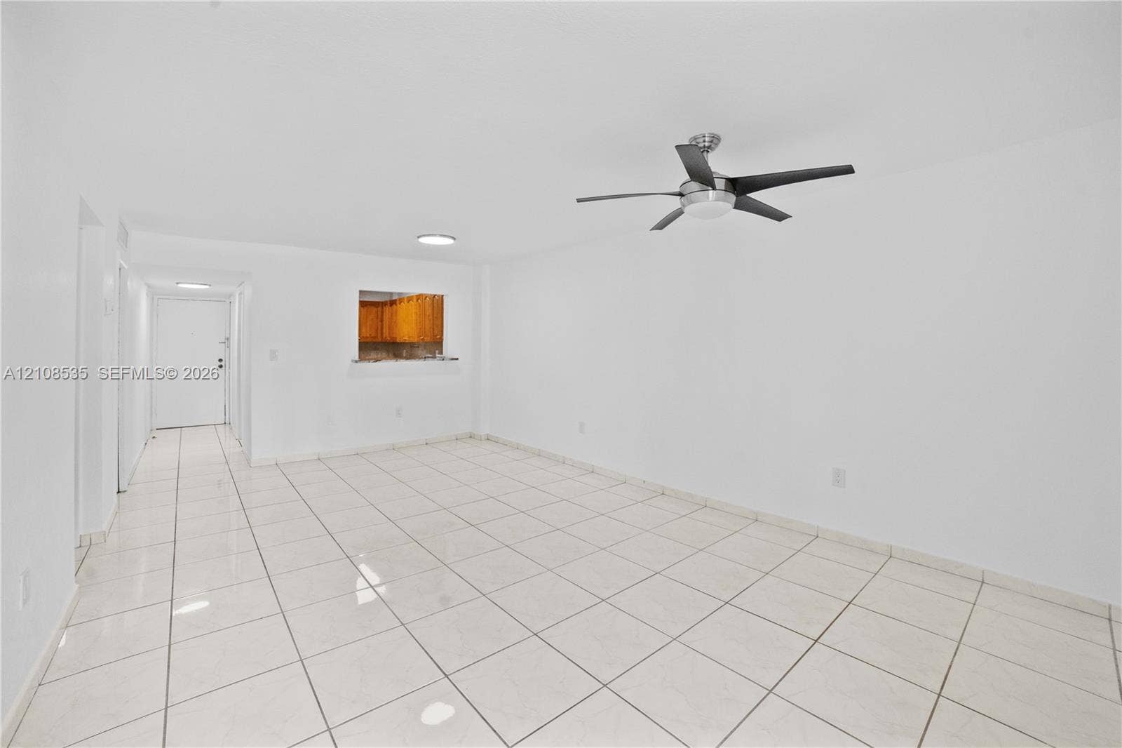 Interior space featuring neutral white walls, ceramic tile flooring, a brushed metal ceiling fan with integrated lighting, and a pass-through opening