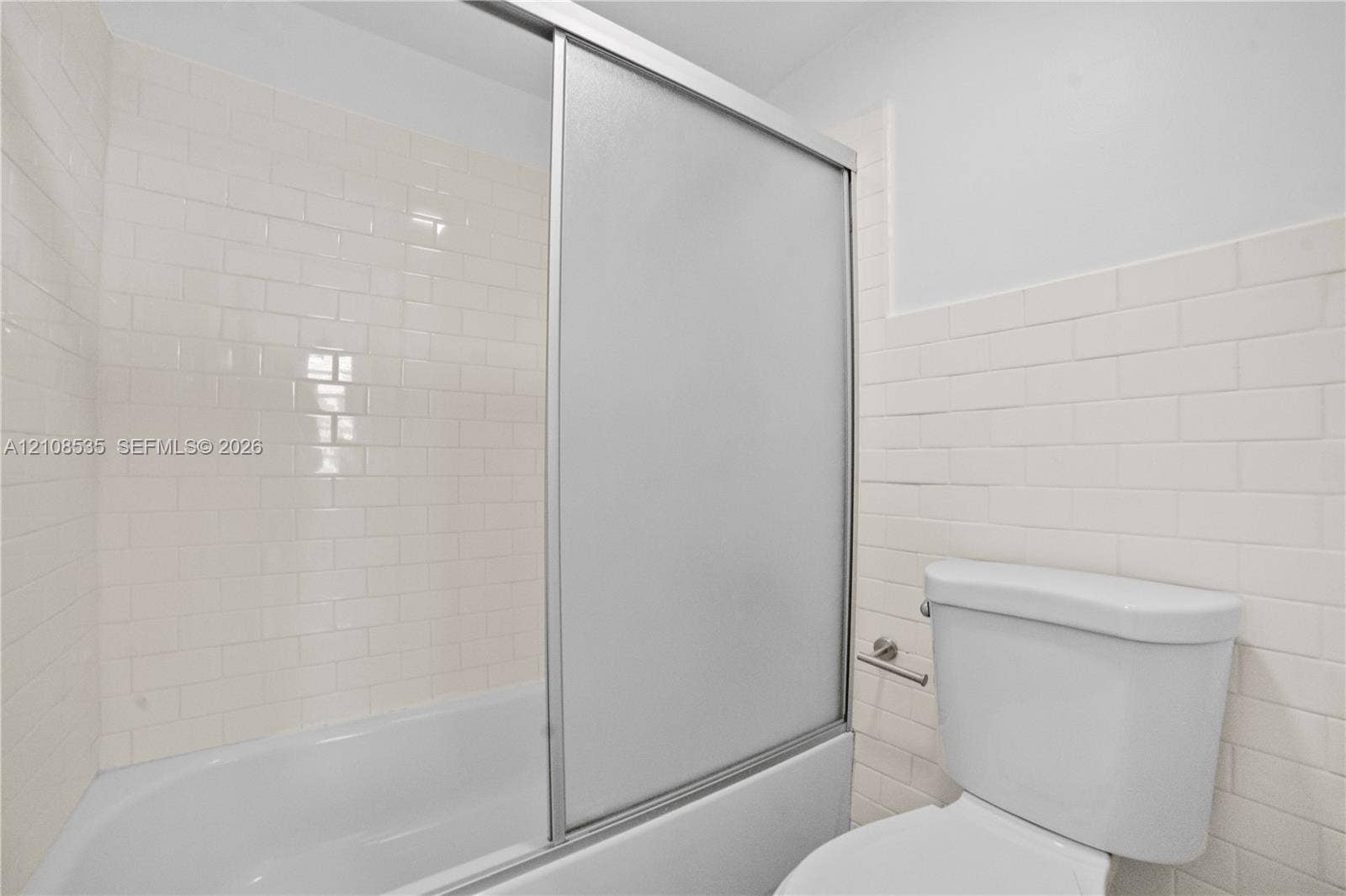 Full-height white subway tile surround, integrated bathtub, frosted glass sliding shower enclosure, and standard porcelain toilet