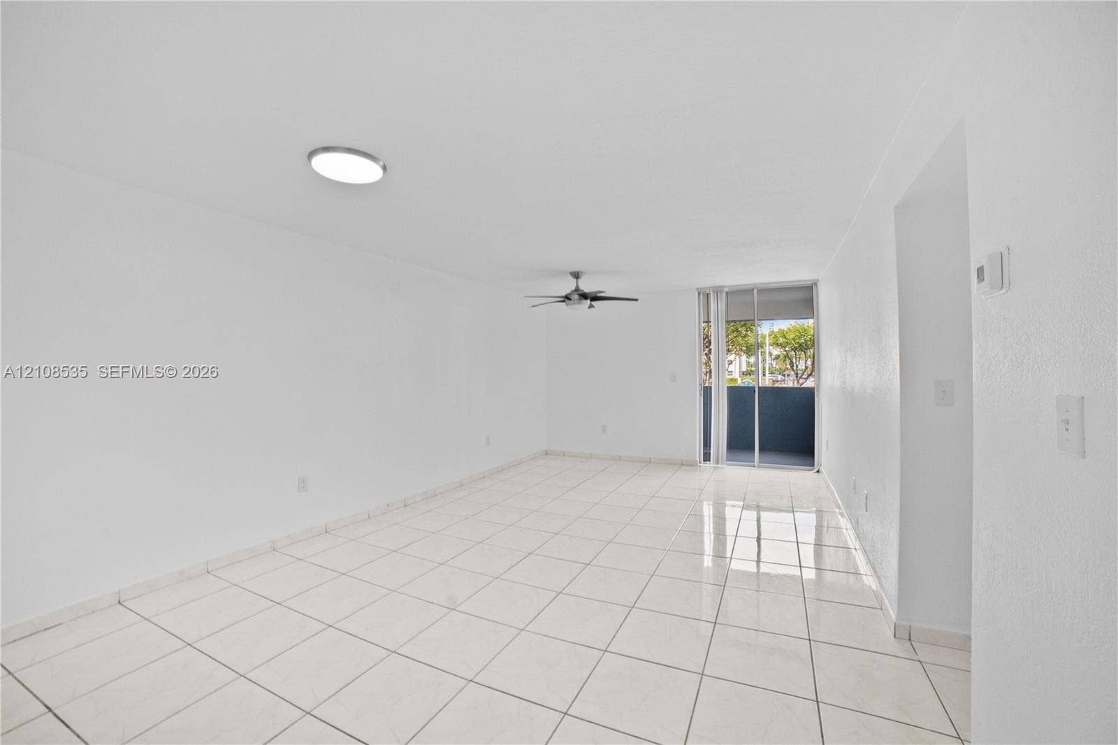 Neutral-toned tile flooring, ceiling-mounted flush lighting, multi-blade ceiling fan, and sliding glass doors with exterior access