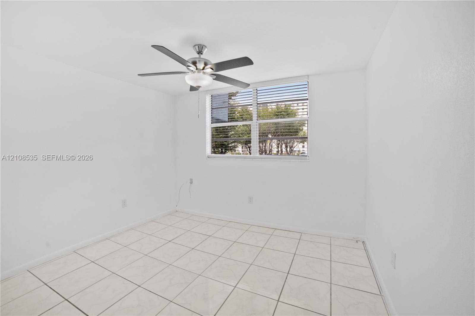 Neutral interior space featuring white tiled flooring, a multi-blade ceiling fan with integrated light fixture, and horizontal window blinds