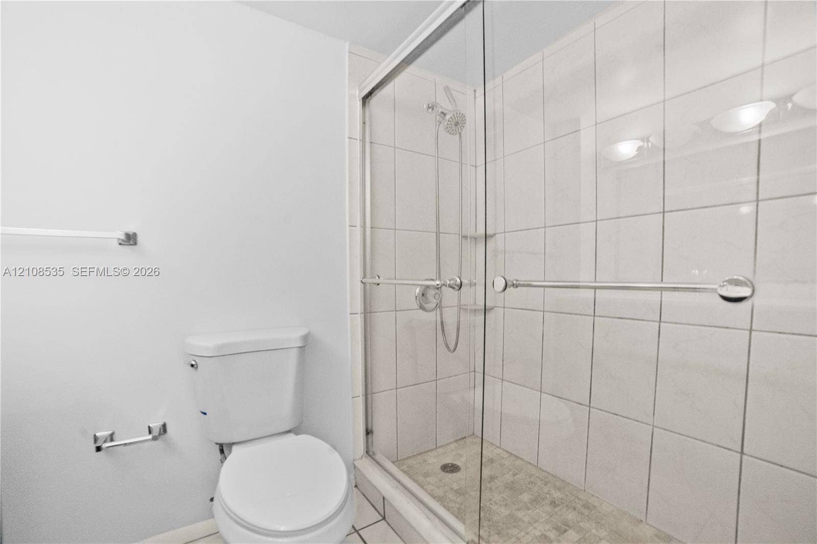 Walk-in shower with floor-to-ceiling tile surround, glass sliding door, integrated handheld shower fixture, and a stone-texture shower floor