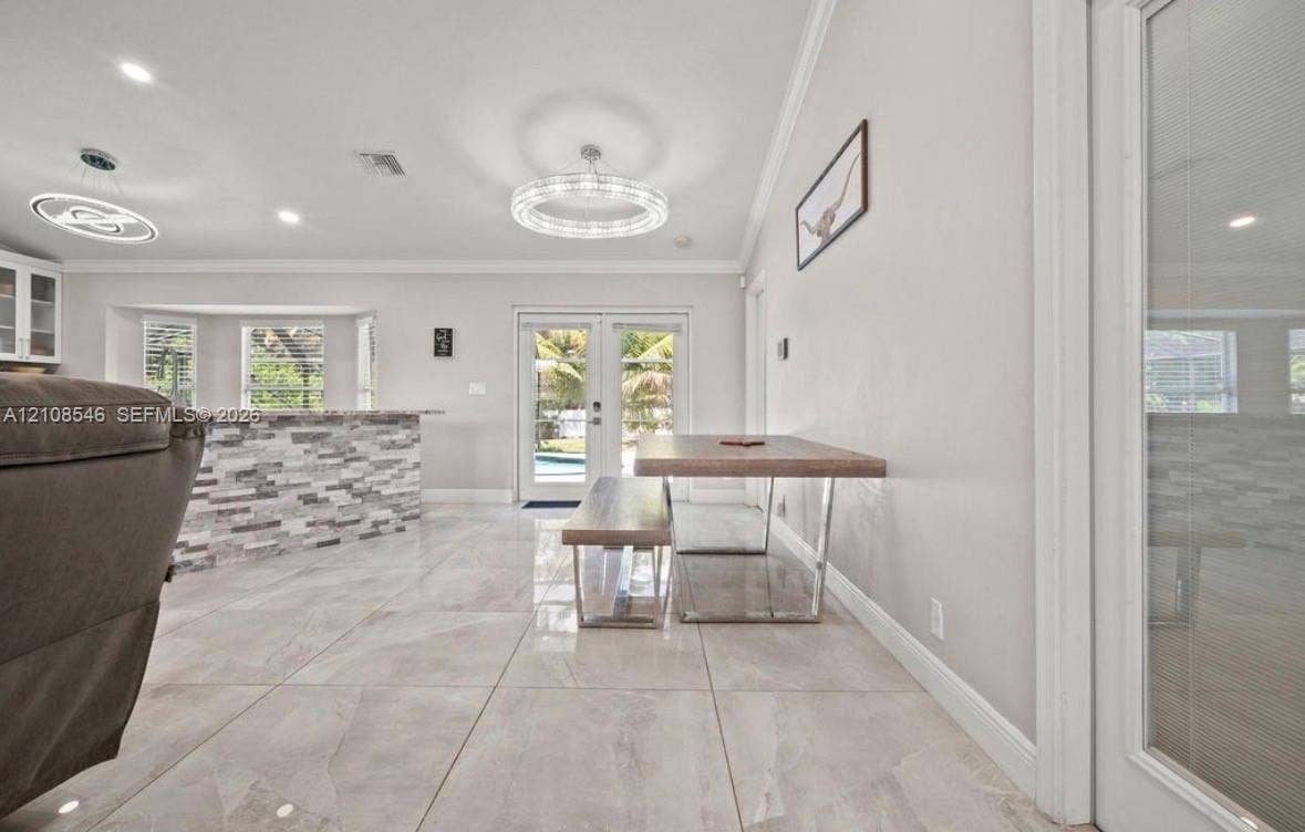 Large-format tile flooring, tiered tray ceiling, circular modern LED light fixtures, stone-veneer kitchen island, and French doors