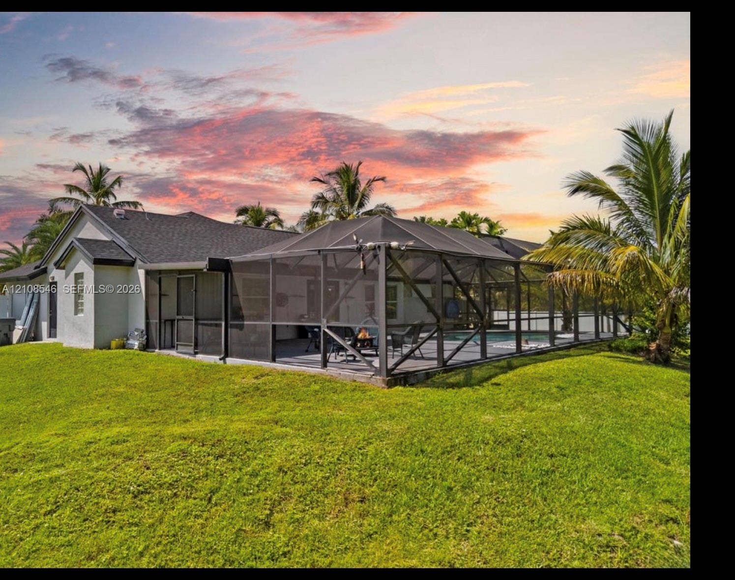 Exterior featuring a screened-in lanai, concrete-tiled roofing, manicured lawn, and mature palm trees