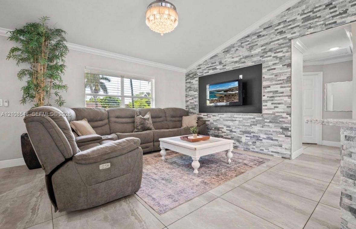 Living area featuring a vaulted ceiling, floor-to-ceiling split-face stone accent wall, large-format tile flooring, and a crystal-style chandelier