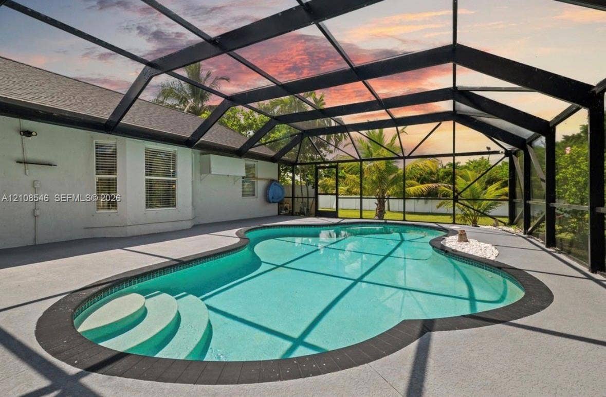 Screen-enclosed pool area featuring a freeform swimming pool, integrated shallow-water entry steps, textured concrete decking, and a dark metal frame structure