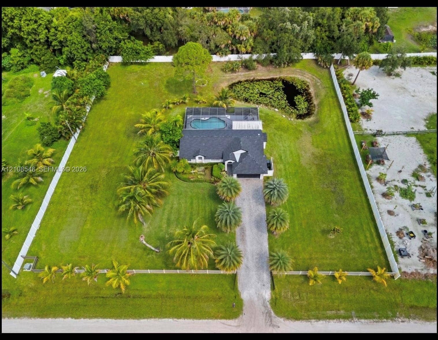 Expansive lot featuring a fenced perimeter, a swimming pool with a screened enclosure, a private pond, and extensive palm tree landscaping