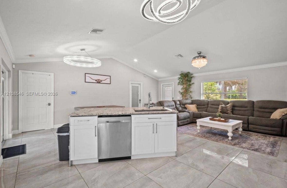 Open-concept living space featuring vaulted ceilings, oversized tile flooring, white cabinetry with stone countertops, stainless steel dishwasher, and contemporary circular chandelier lighting