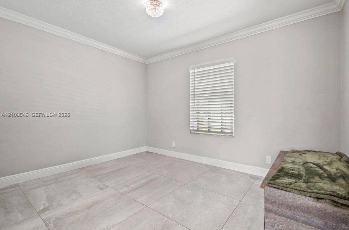 Neutral-toned room featuring large-format stone-finish floor tiling, crown molding, and a single window with horizontal blinds