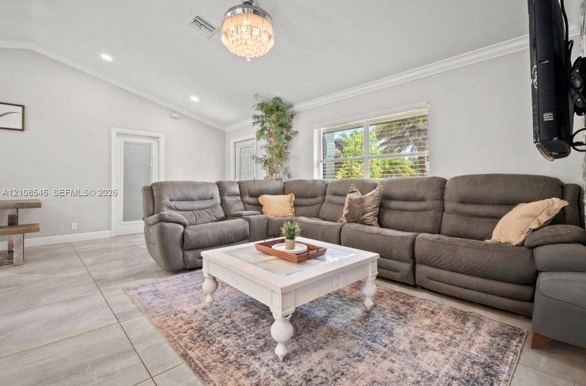 Living space featuring vaulted ceilings, oversized tile flooring, crown molding, recessed lighting, and a crystal chandelier