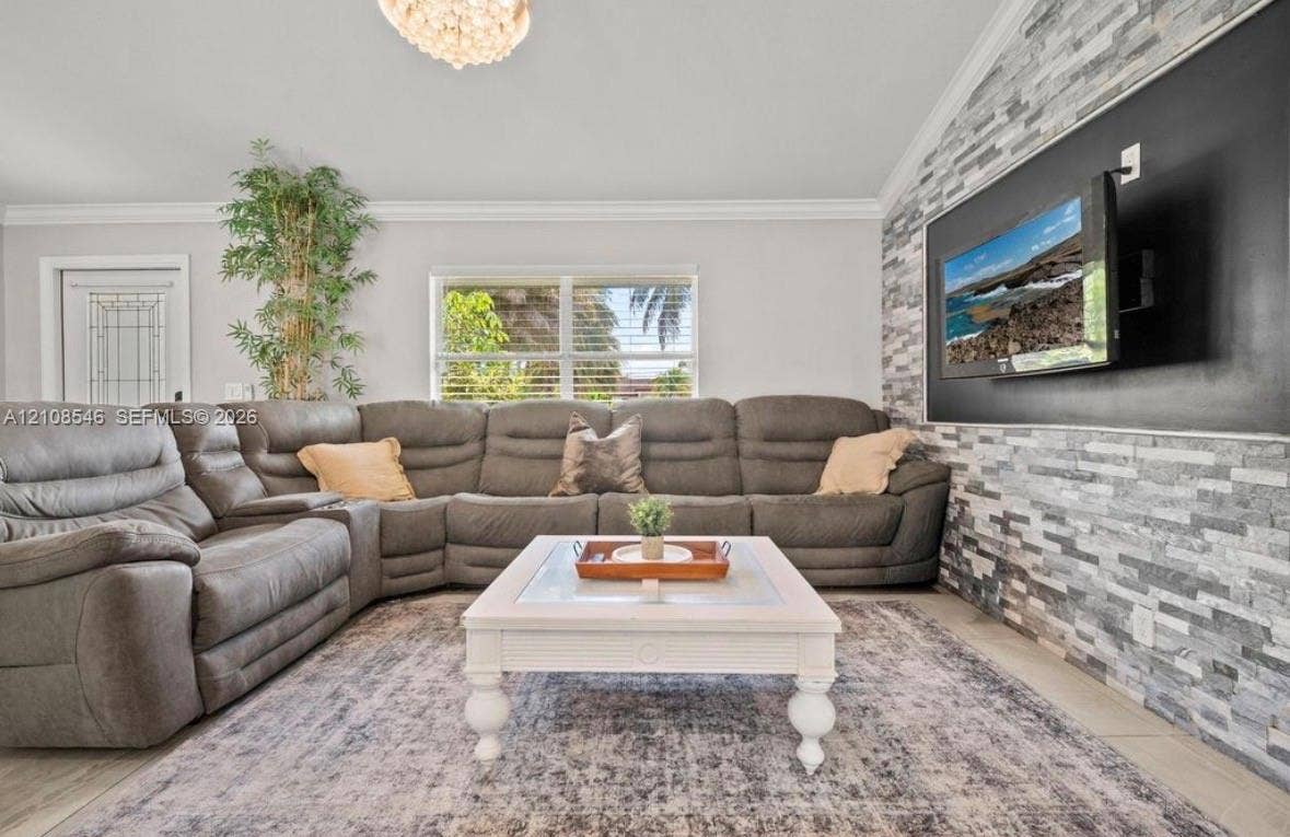 Vaulted ceiling featuring a decorative chandelier, stacked stone accent wall, and crown molding